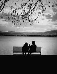 Rear view of couple sitting on lake against sky