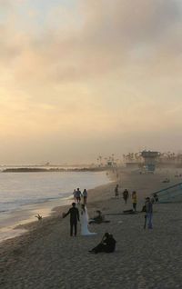 People walking on beach against sky during sunset