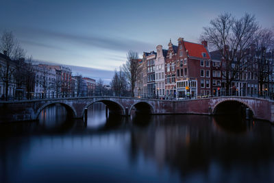 Bridge over river by buildings against sky in city