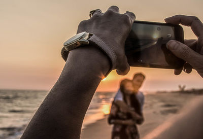 Midsection of man using mobile phone against sky during sunset