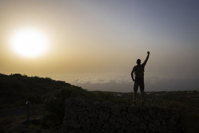 Rear view of man with arms outstretched standing on mountain against sky during sunset