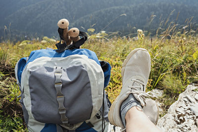 Hiking backpack, trekking poles and legs in sports shoes of young woman resting in mountain hike