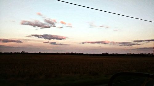 Road passing through field at sunset