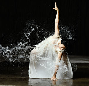 Woman splashing water against black background