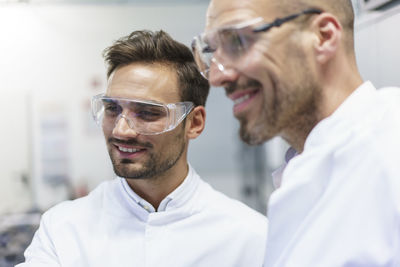 Smiling male technicians looking away at illuminated laboratory