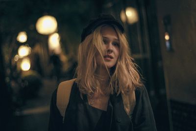 Portrait of young woman with blond hair standing outdoors at night