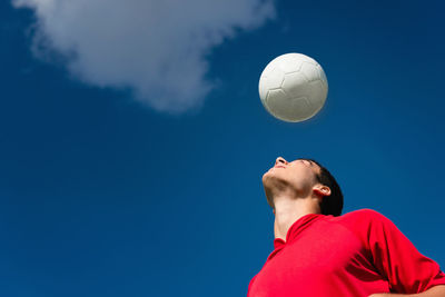 Low angle view of man playing with soccer ball against blue sky during sunny day