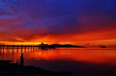 Silhouette man fishing in sea against orange sky