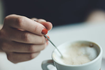 Close-up of hand holding coffee cup and spoon
