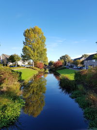 Canal amidst trees and buildings against blue sky