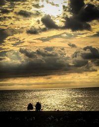 Silhouette people on beach against sky during sunset