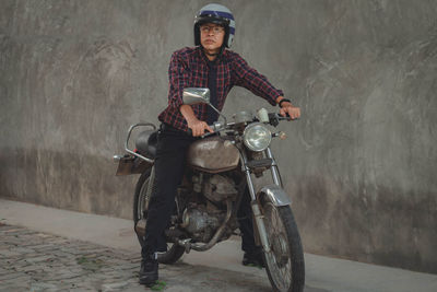 Portrait of man riding motorcycle on road against wall