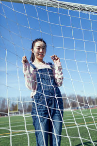 Portrait of woman standing by net on field during sunny day