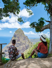 Rear view of woman sitting on rock against sky