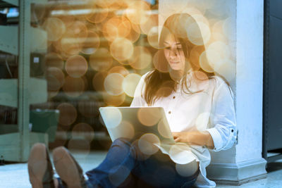 Double exposure of young woman using laptop with defocused light at night