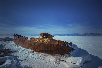 Abandoned boat on sea shore during winter against sky