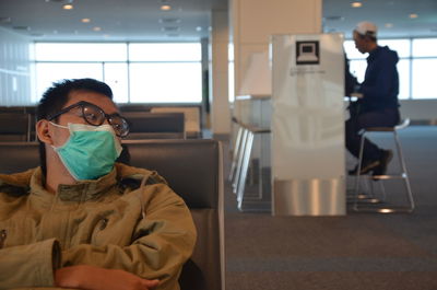 Close-up of man wearing mask while sitting at airport departure area