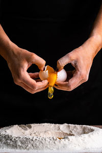 Close-up of hand holding ice cream cone against black background