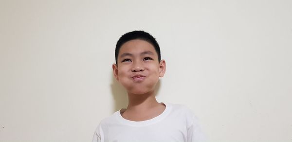 Close-up of boy making face while looking away against white wall