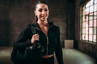 Portrait of smiling young woman standing against wall