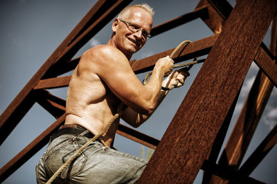 Low angle portrait of shirtless man standing on metallic structure