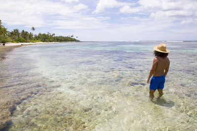 Man with curly hair and golden hat in rocky beach with palm trees