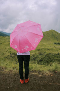 Rear view of woman standing on pink umbrella against sky