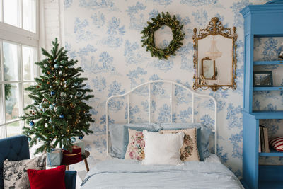Pillows on the bed, a christmas wreath on the wall, a christmas tree by the window
