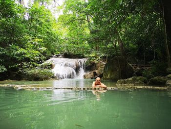 Man in waterfall against trees in forest