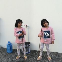 Twins standing against white wall