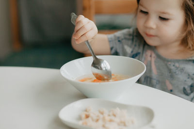 A little girl is sitting at the kitchen table eating soup. high quality photo