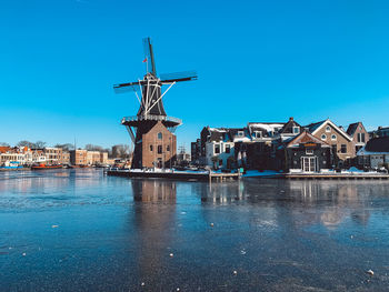Buildings by river against clear blue sky