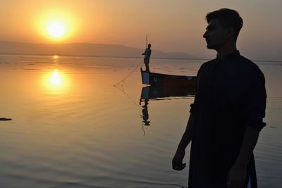 Silhouette man fishing in sea against sky during sunset