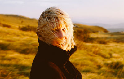 Side view of young woman with tousled hair on field during sunset