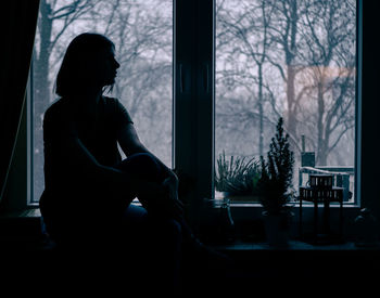 Silhouette woman sitting by window at home