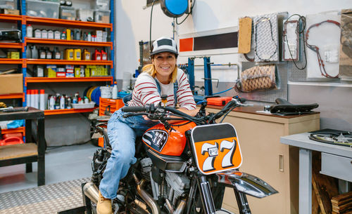 Portrait of mechanic woman leaning over motorcycle on factory