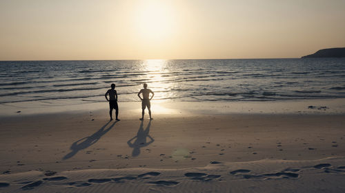 Silhouette people standing on beach against clear sky during sunset