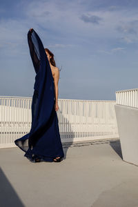 Woman standing on railing by sea against sky