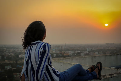Woman looking at cityscape against sky during sunset