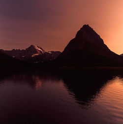 Scenic view of lake by silhouette mountains against sky during sunset