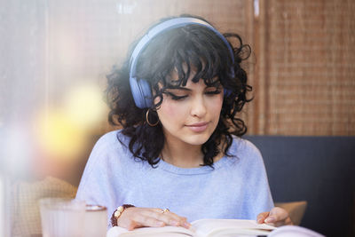 Young woman wearing headphones listening to music or podcast while reading book