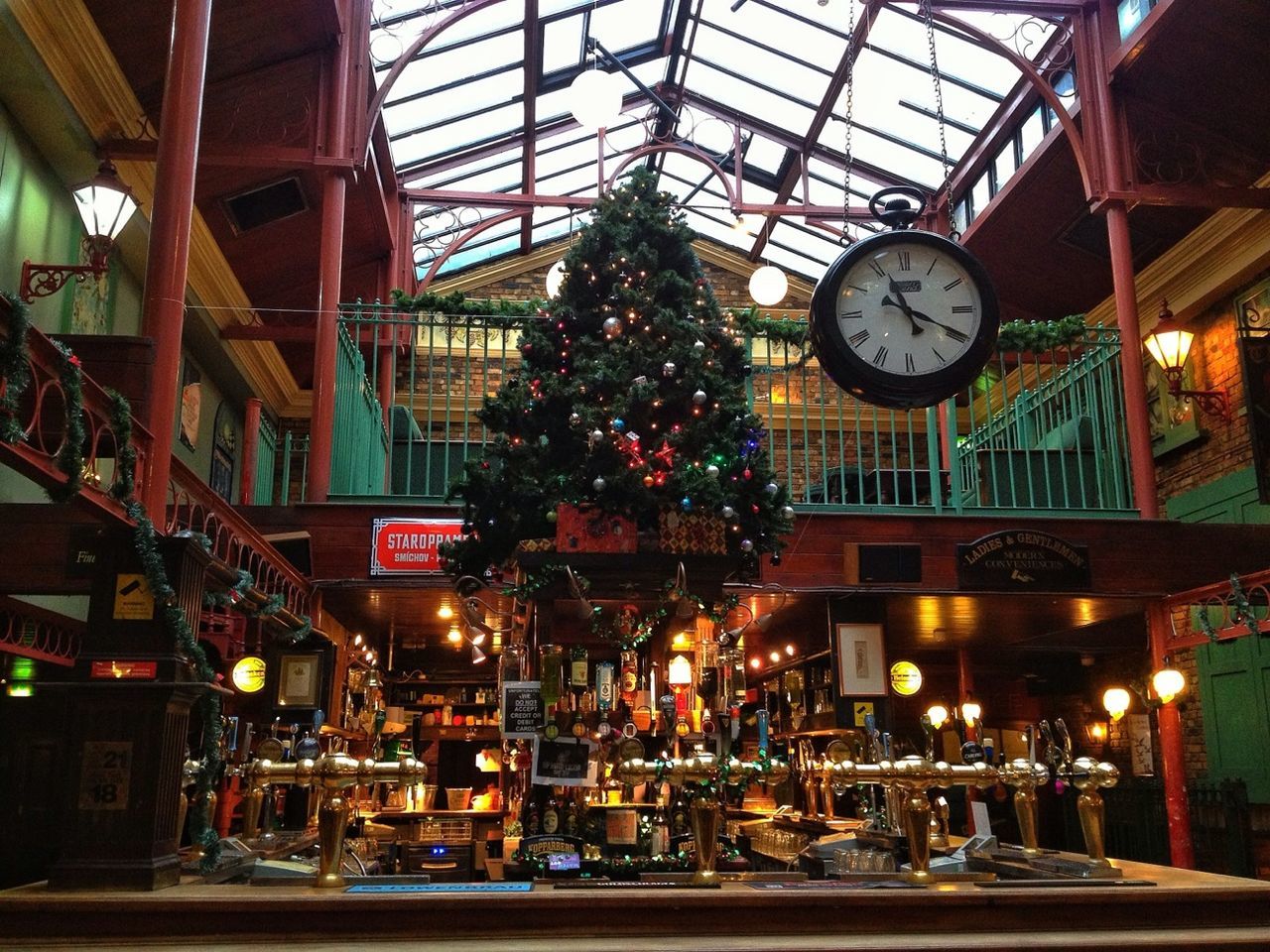 indoors, illuminated, architecture, glass - material, built structure, ceiling, window, table, lighting equipment, low angle view, restaurant, incidental people, hanging, clock, no people, decoration, transparent, food and drink, circle, time