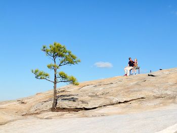 Low angle view of people on tree against clear blue sky