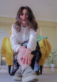 Low angle portrait of young woman sitting on chair at home