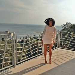 Woman standing on toe by railing at balcony against sky