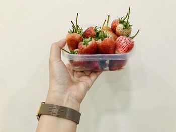 Cropped image of hand holding strawberry against white background