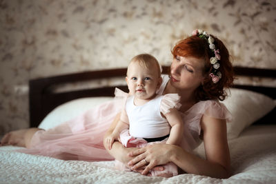 Gentle mother and daughter on the bed in a real room, the concept of motherhood and affection