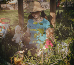 Young woman playing with dolls while sitting by plants in lawn