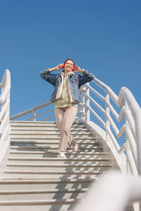 Low angle view of woman standing on staircase against clear blue sky