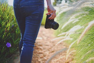 Midsection of woman holding camera while standing amidst plants